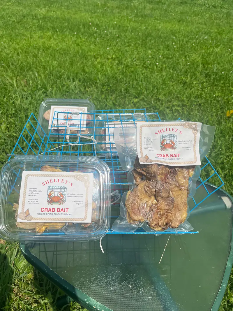 Shelley's Crab Bait in both packaging types — a rigid tub and a vacuum-sealed pouch — on a wheelbarrow with a crab trap